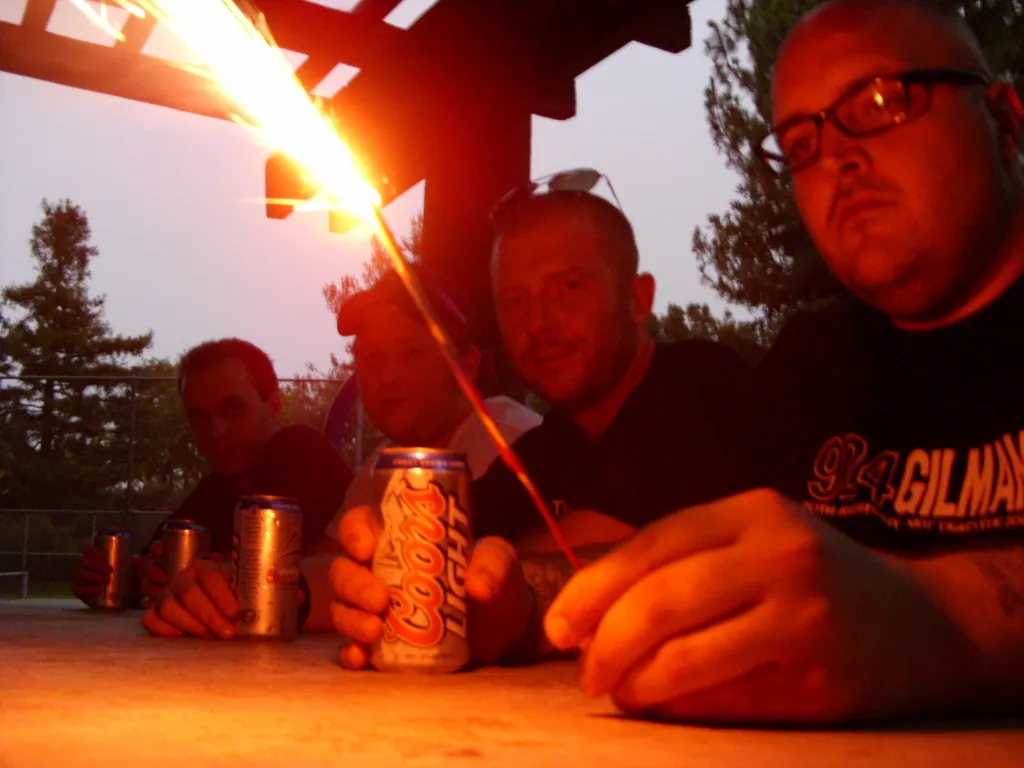 SecondShot members sitting at an outdoor picnic table at dusk with a sparkler burning